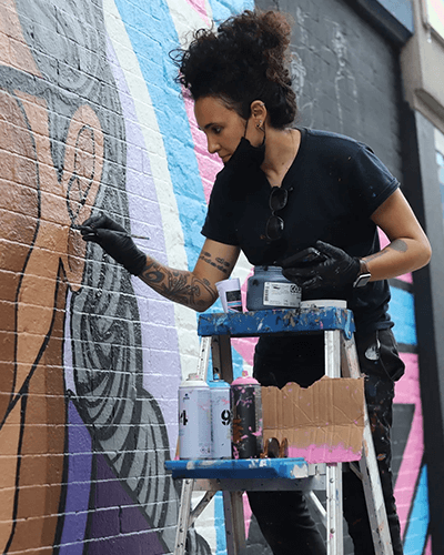 Artist S. Kirk standing on a ladder painting mural