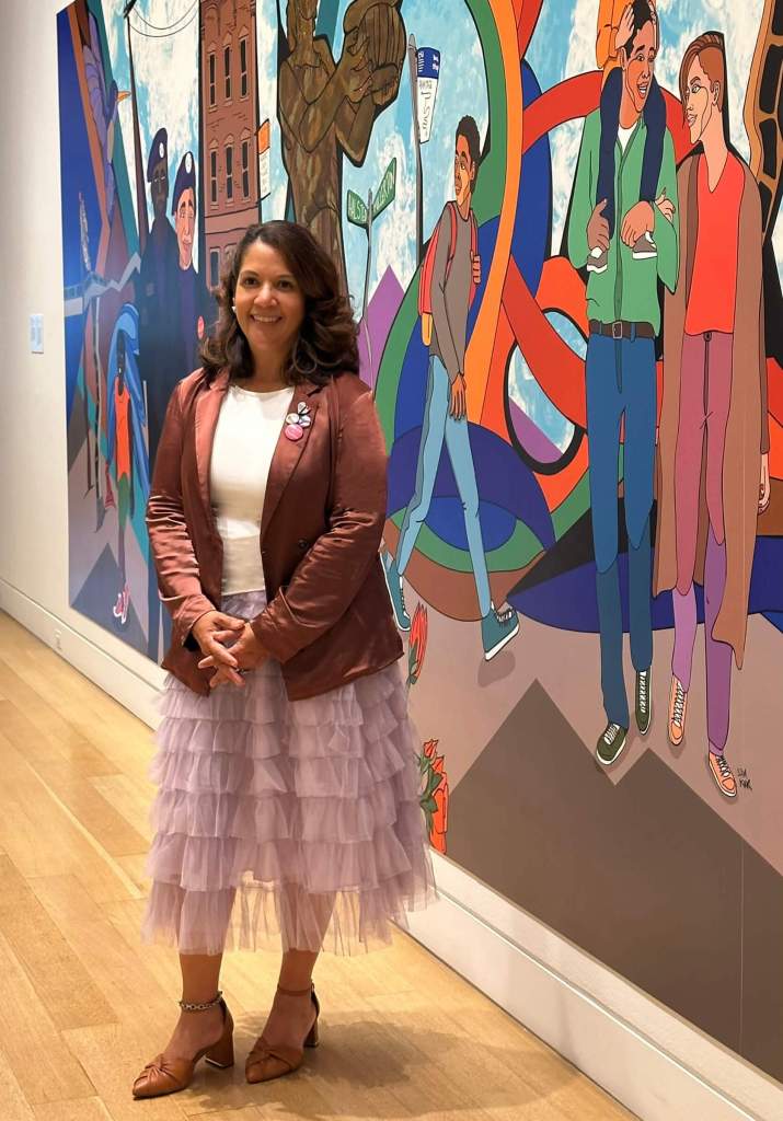 Dr. Lazu standing in front of a mural by Sam Kirk. 